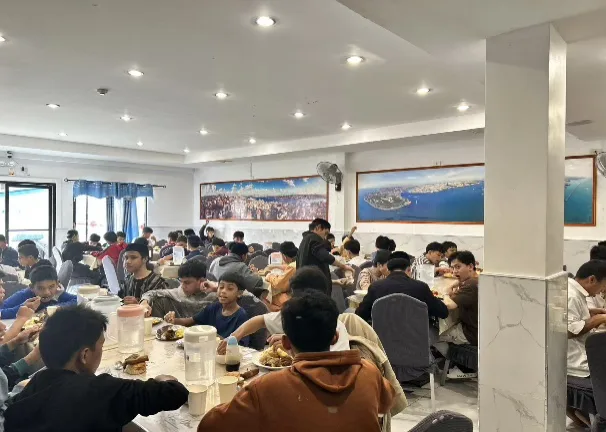 A dining hall full of students eating at long tables.